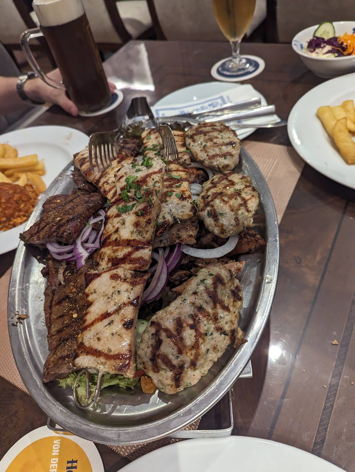 Grillplatte mit verschiedenen Fleischsorten wie Souvlaki und Bifteki, serviert auf Metallteller mit roten Zwiebeln.