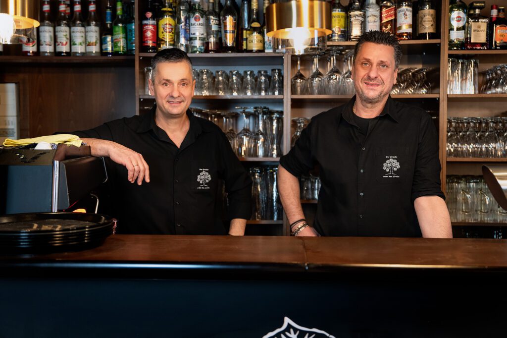 Zwei Besitzer des Restaurants „Der Grieche unter den Linden“ hinter der Bar – freundlich, professionell und gastfreundlich.