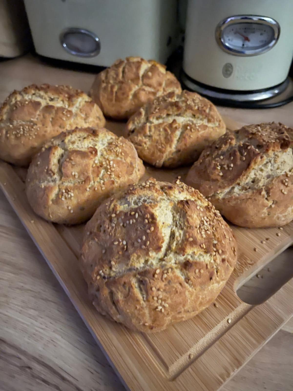 Frisch gebackene Brötchen mit Sesam auf einem Holzbrett in einer heimischen Küche.